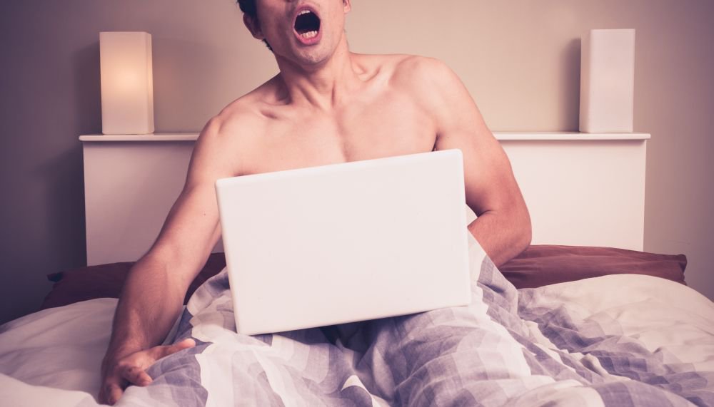 Young man is sitting in bed and watching pornography on laptop