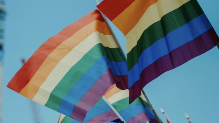 Three rainbow Pride flags against a blue sky.