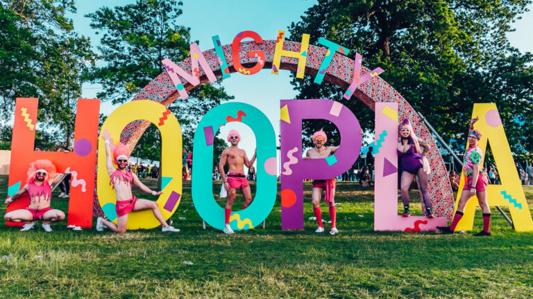 A group of festival goers pose in front of a Mighty Hoopla sign