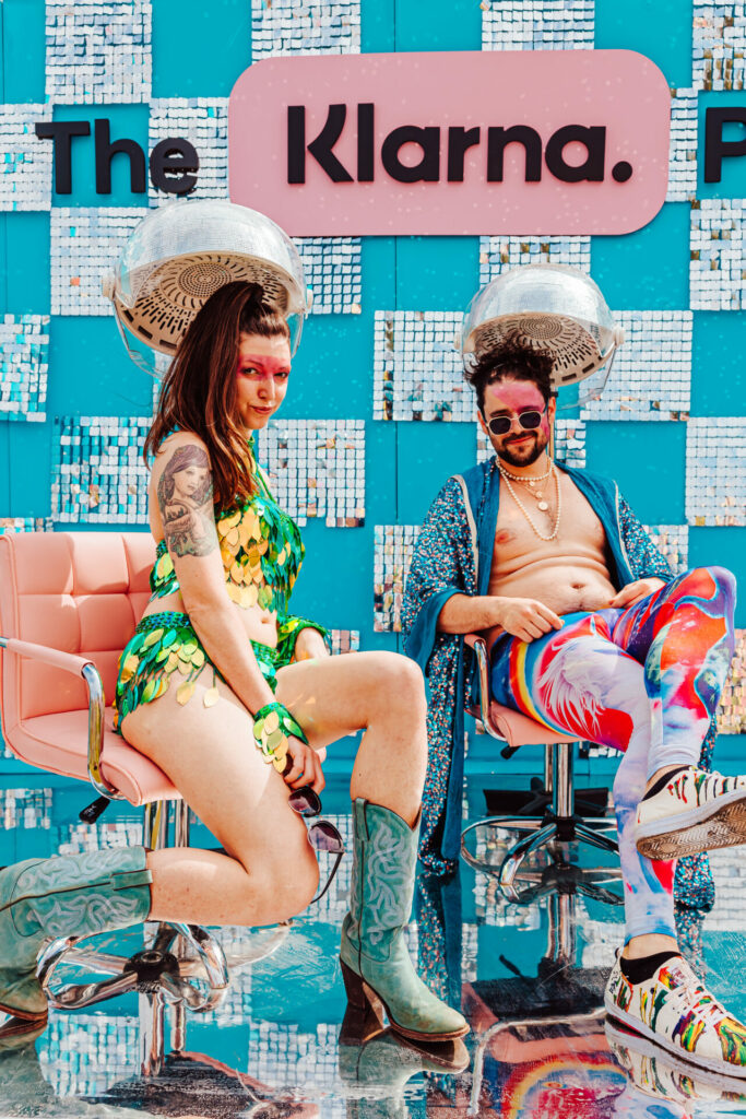 Two people sit under hairdryers in the Klarna Parlour at the Mighty Hoopla festival