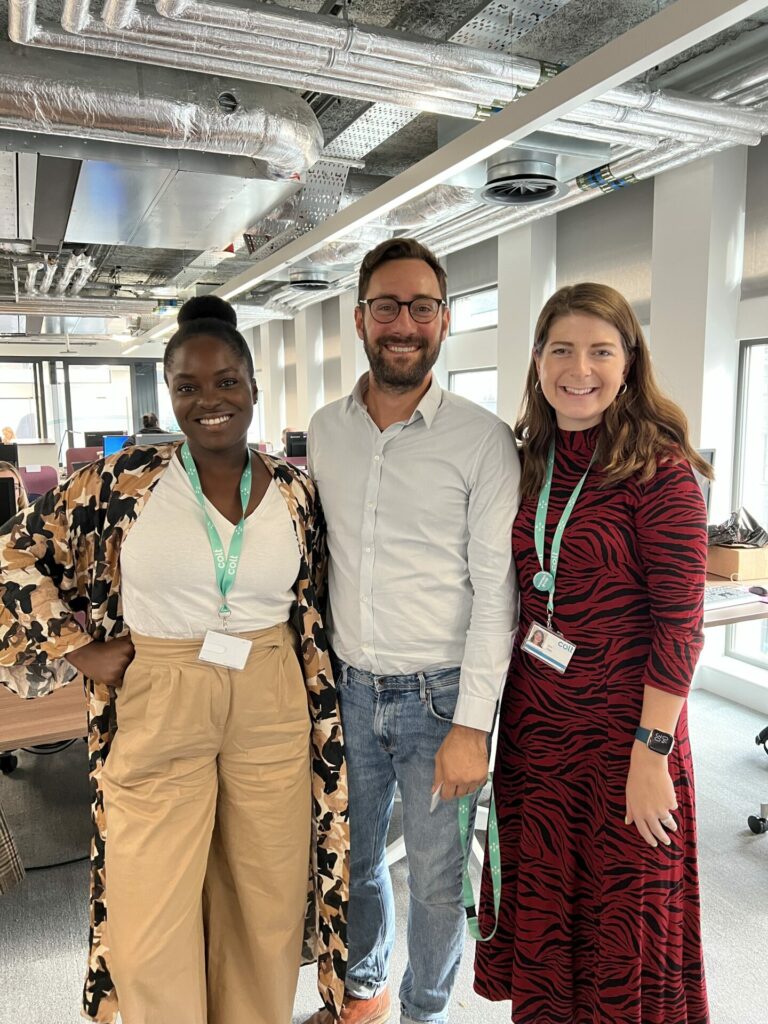 A group of three people stand inside an office with corporate lanyards around their necks