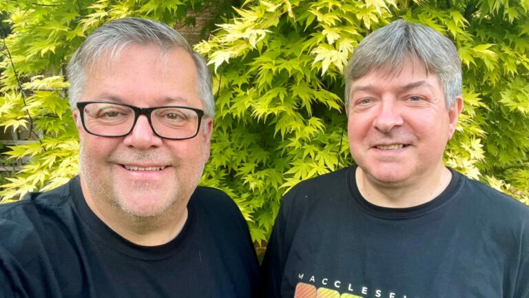 Two men looking into the camera smiling with a bush behind them