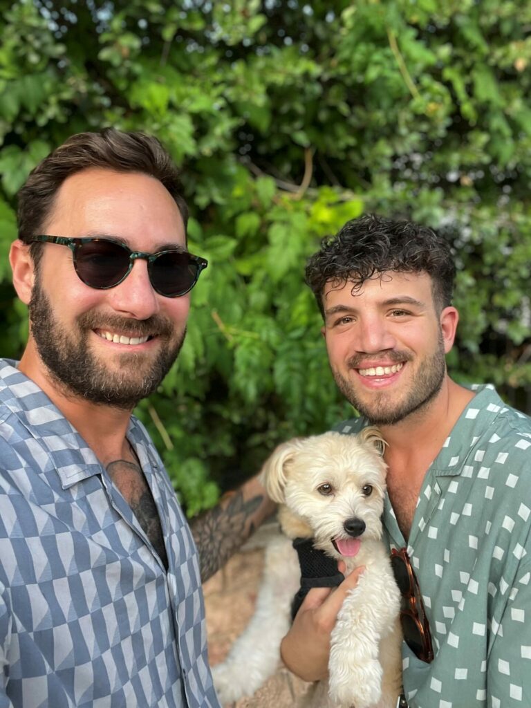 Two men pose with a dog in the middle of them