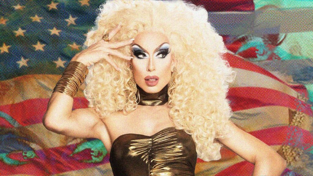 Drag queen Alaska with large blonde hair in front of a US flag
