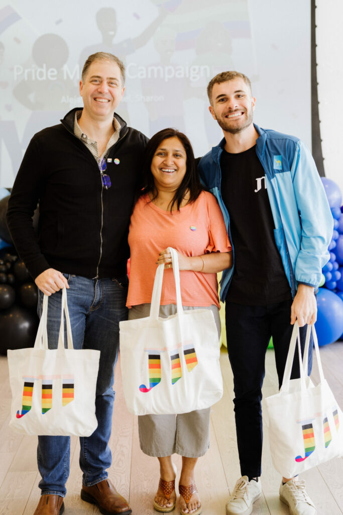 Three people hold tote bags and smile into the camera