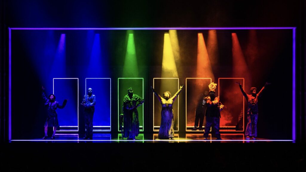 A Strange Loop US production: several actors on stage, each under a different colour light of the rainbow. Purple on the left to red on the right.