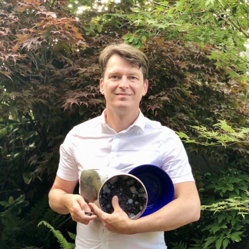 portrait image of Bruno Vinel, white man with brown hair wearing a white shirt. he's holding a variety of ceramics.