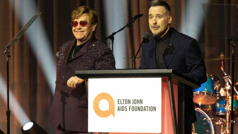 Elton John and David Furnish standing on an Elton John AIDS foundation podium