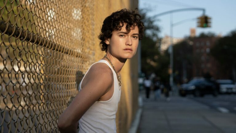 headshot of Lío Mehiel in the sun standing against a chain link fence.