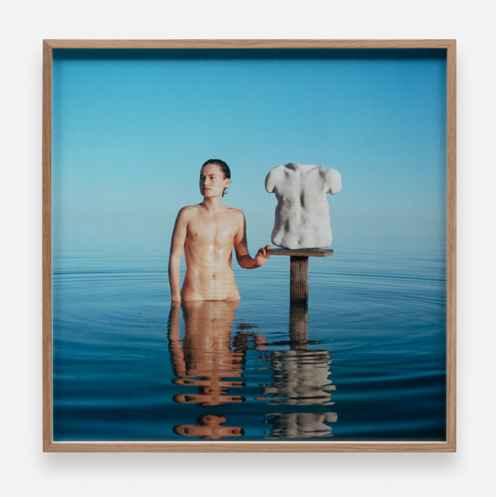 Lío Mehiel standing in a lake beside a sculpture of their chest. The piece titled: Angels of a drowning world.