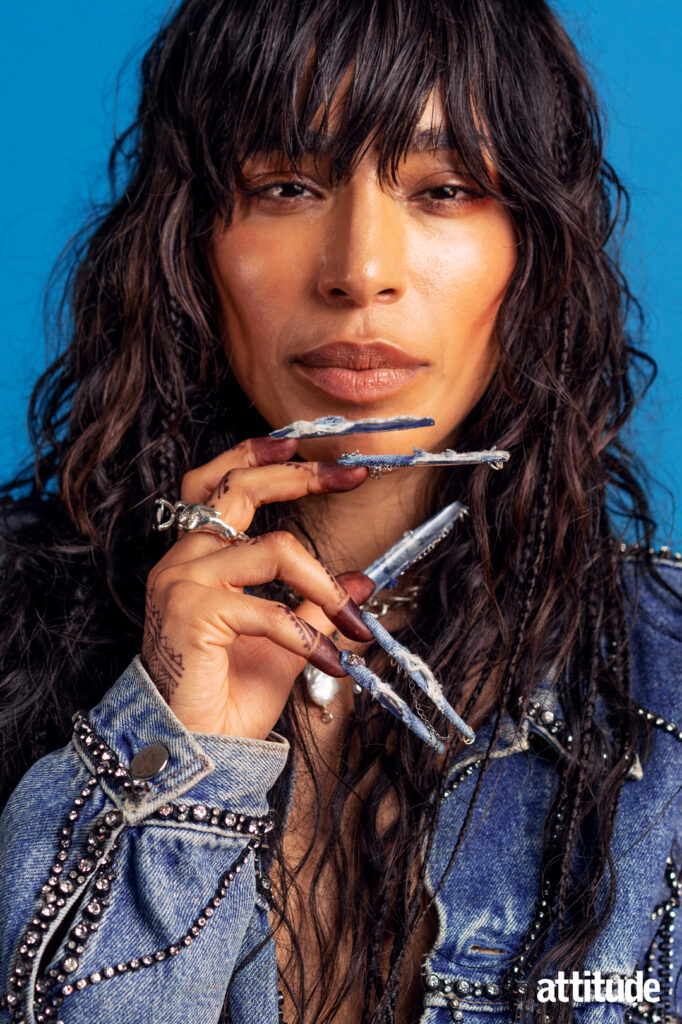 Loreen looking into the camera wearing a denim jacket and long light blue nails.