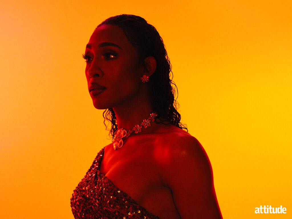 Michaela Jaé Rodriguez wearing a gold glittering dress, standing against a mustard background.