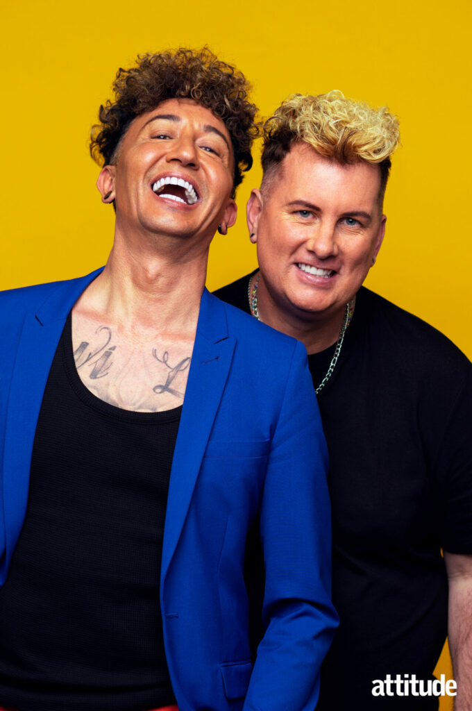 Same-sex couple Michael and Paul posing against a yellow background - both laughing