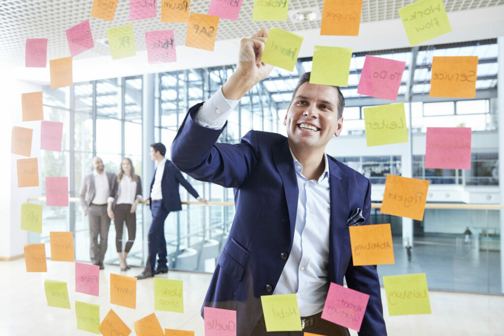 A man stands in front of a glass wall filled with Post-It notes