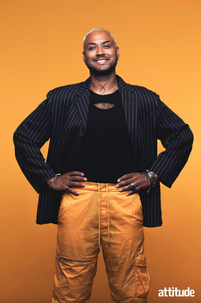 Ryan standing, hands on hips, with mustard cargo trousers and a black pinstripe blazer against a mustard background.