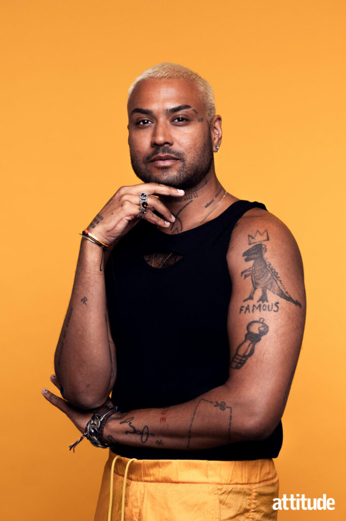 Ryan in a black vest showing several tattoos against a mustard background.