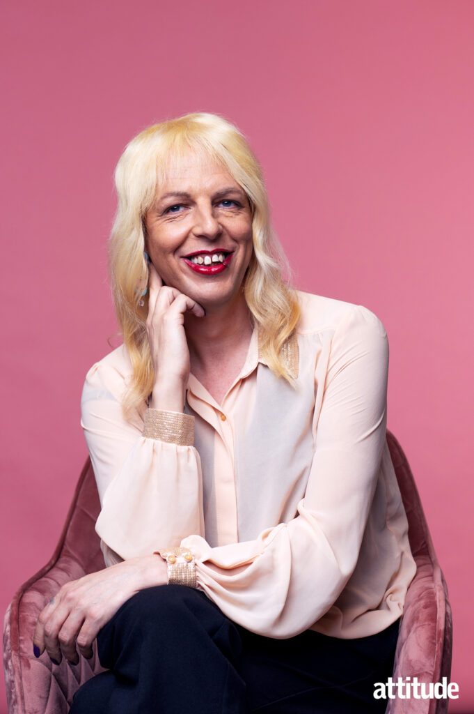Sarah Savage in a pink blouse sitting on a crushed velvet pink chair against a bright pink background.