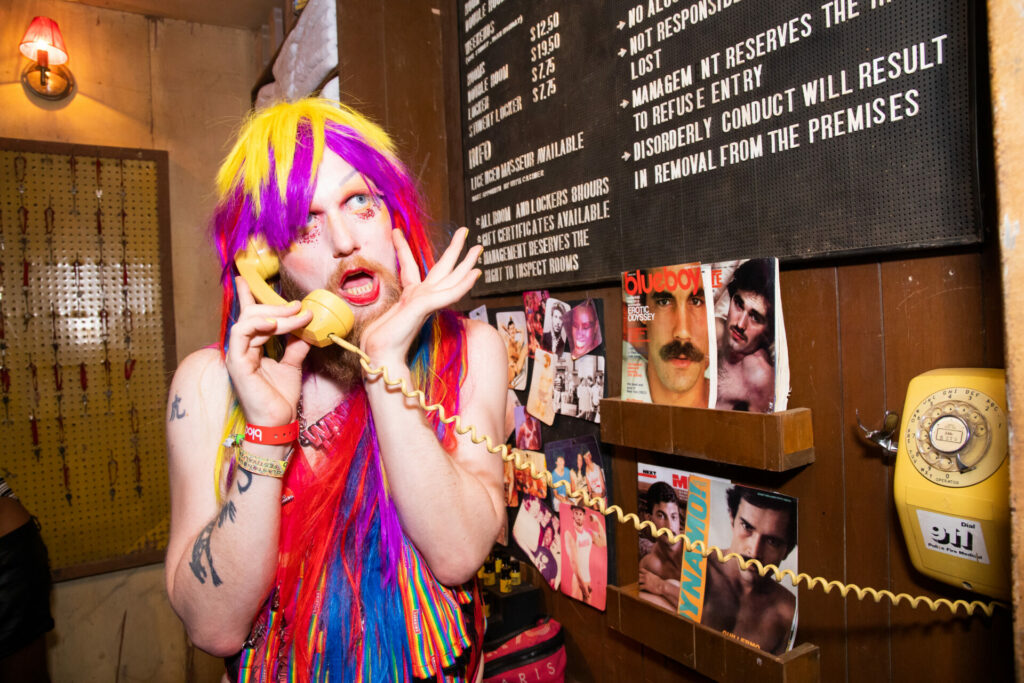 Dressed up person with a colourful wig and clothes on a wall phone