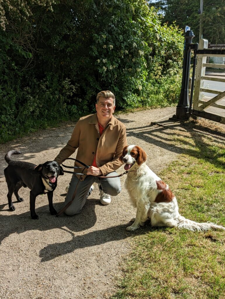 A man kneels on the ground with two dogs