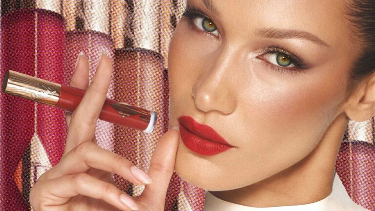 Bella Hadid holds a lipstick to her mouth with a background of lipsticks