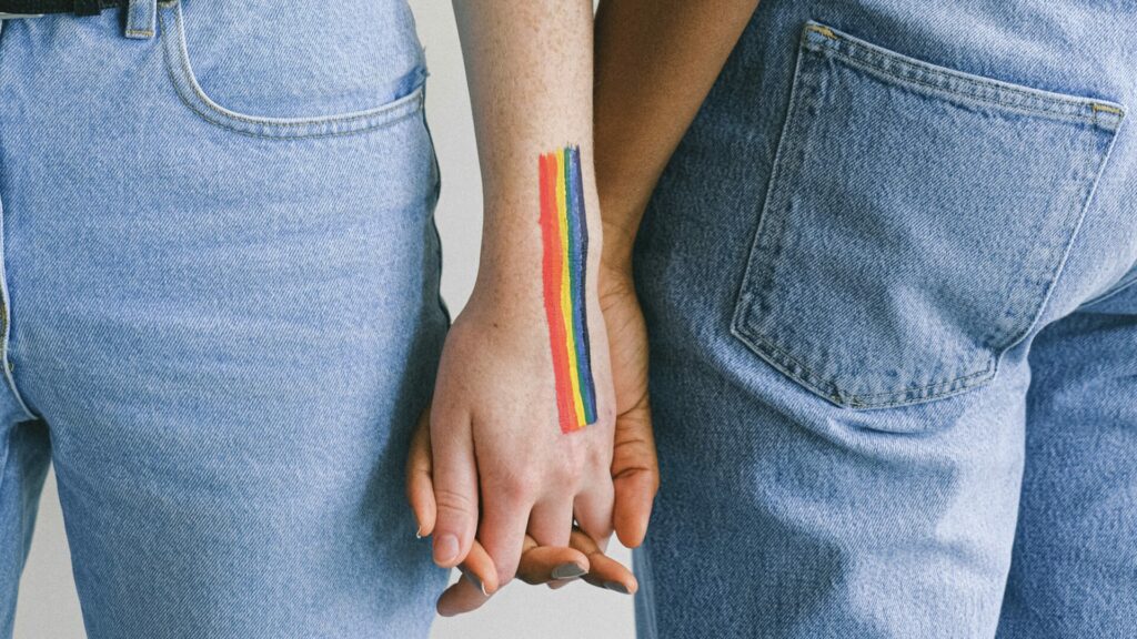 Two people holding hands with a painted rainbow on their skin.