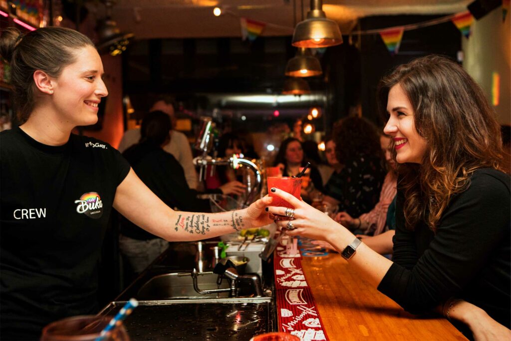 A woman hands a drink across a bar to another woman