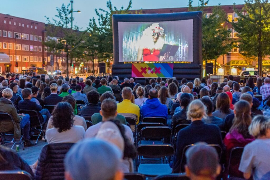 People sit in chairs facing a cinema screen in an outdoor cinema