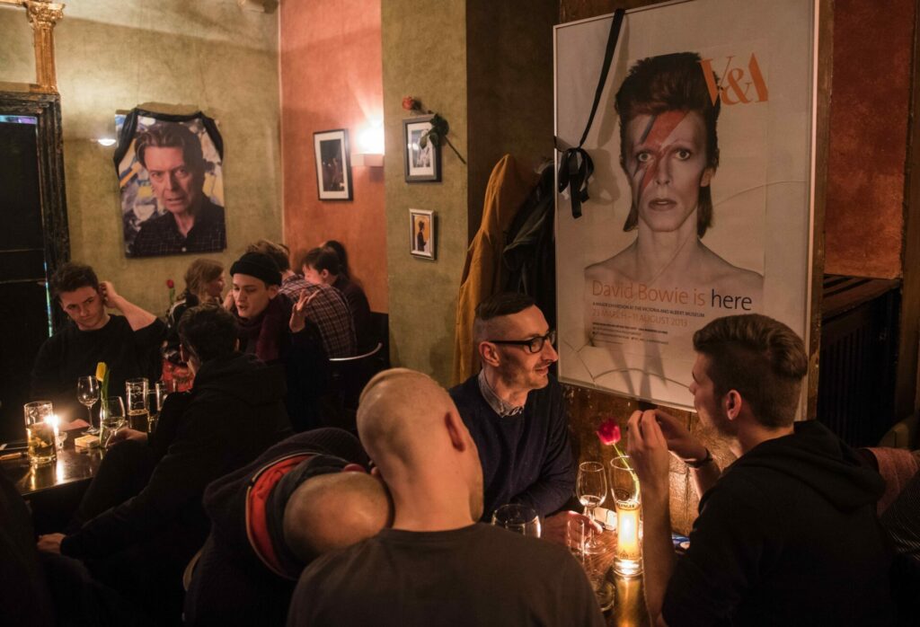 Group of people sitting in a bar with a David Bowie poster in the background