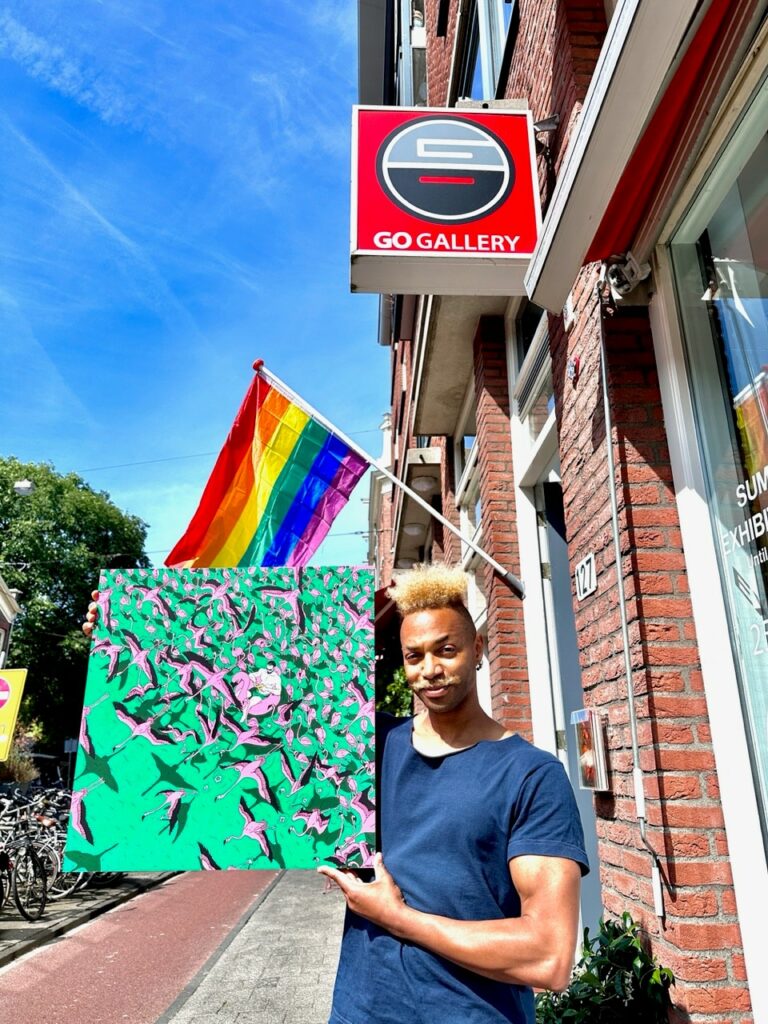 A man stands in front of a building holding a green painting up and looking into the camera