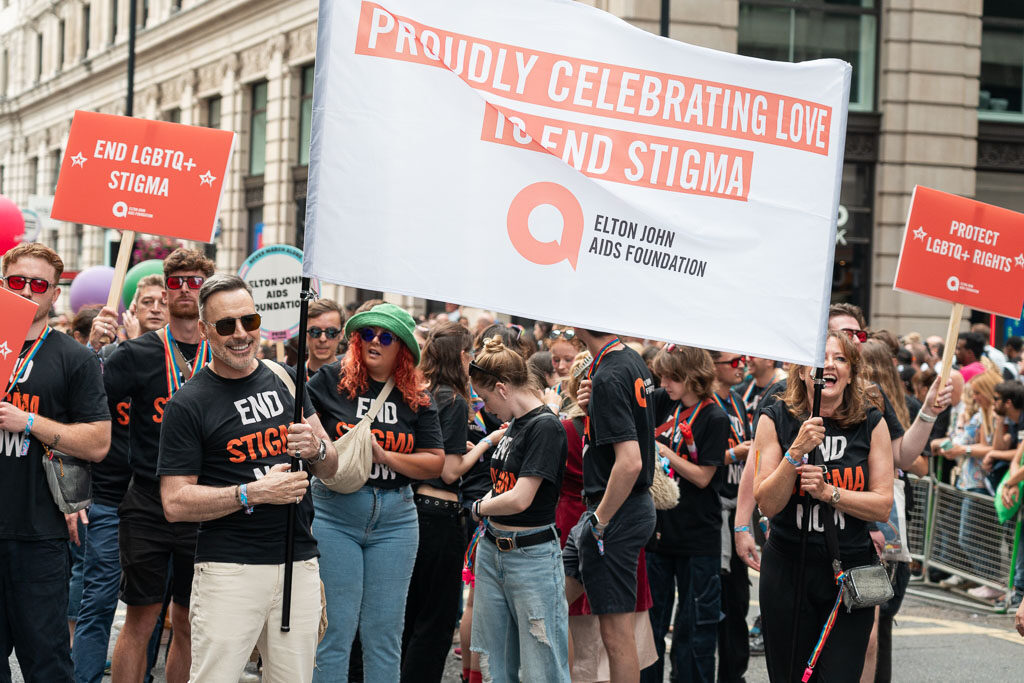 David Furnish and a group of people hold an Elton John AIDS Foundation banner marching during Pride in London