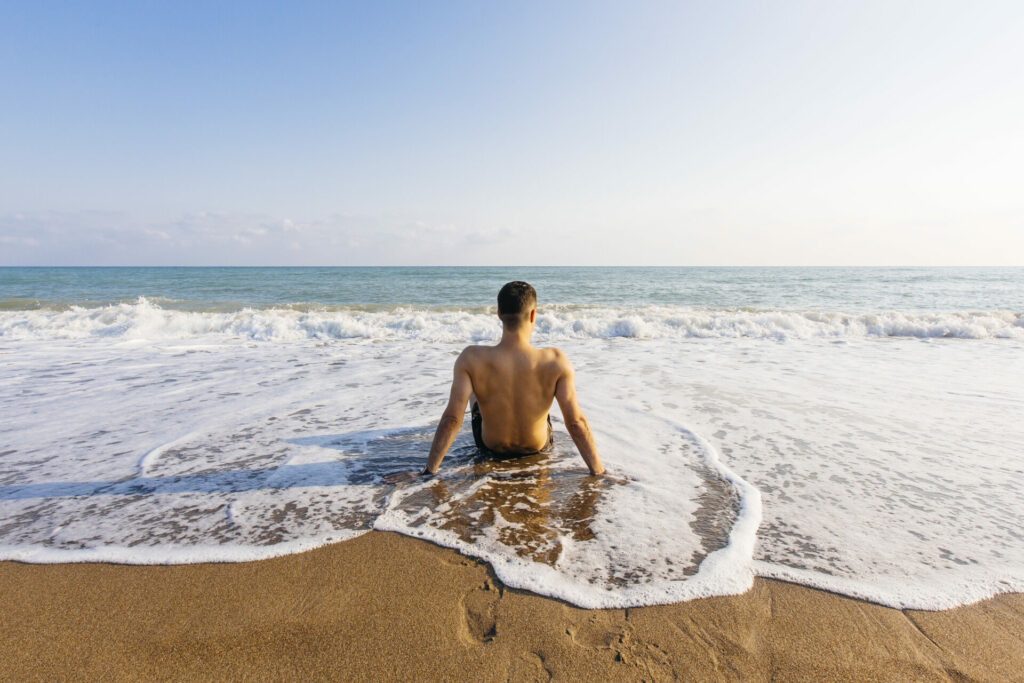 A man sits on a beach with waves surrounding him