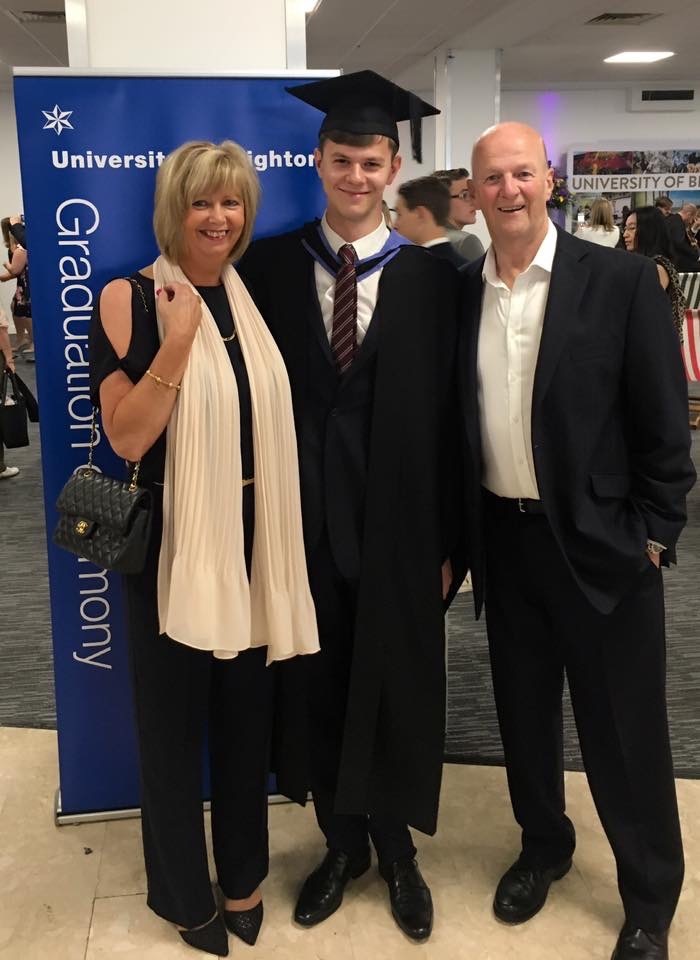 A man in a cap and gown stands in the middle of his parents as they smile and pose