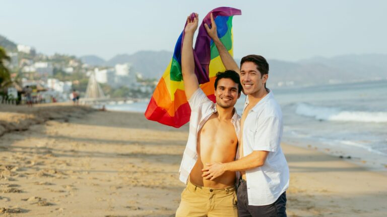 Gay honeymooners pose with a Pride flag on a beach