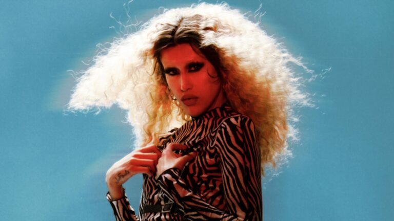 Adore Delano wearing an animal print dress and long blond hair against a blue background
