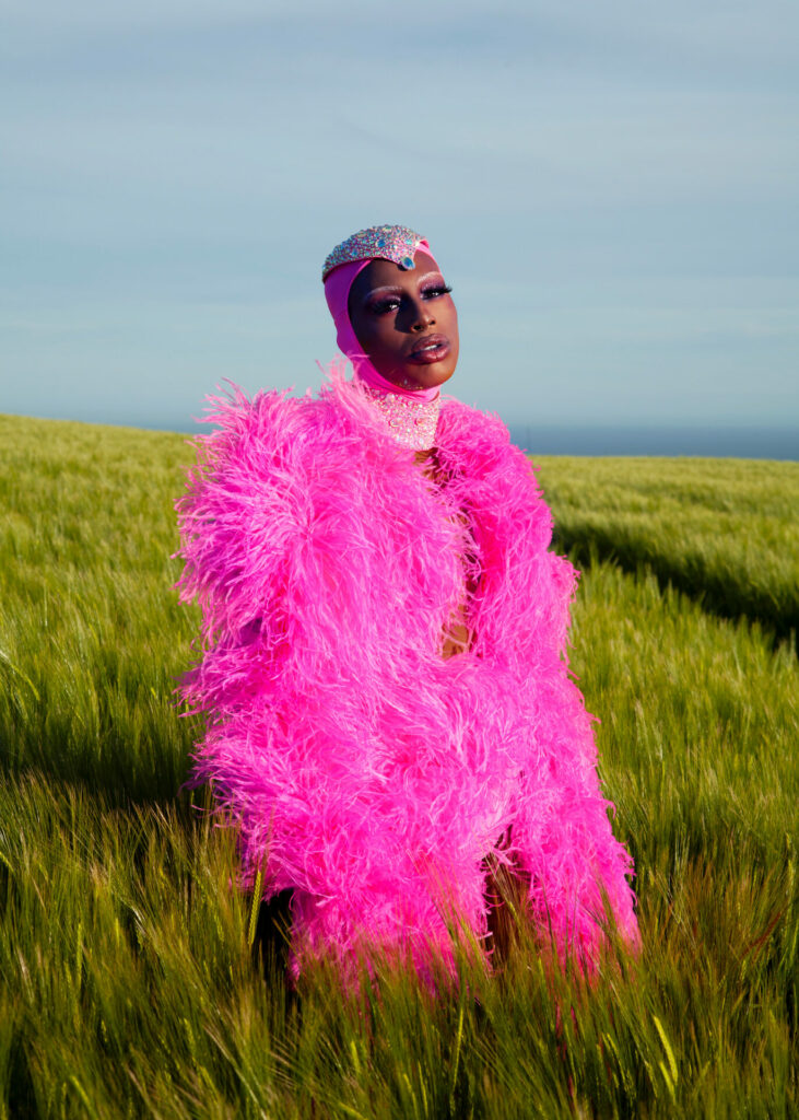 Drag queen Baby dressed in pink stands in a green field