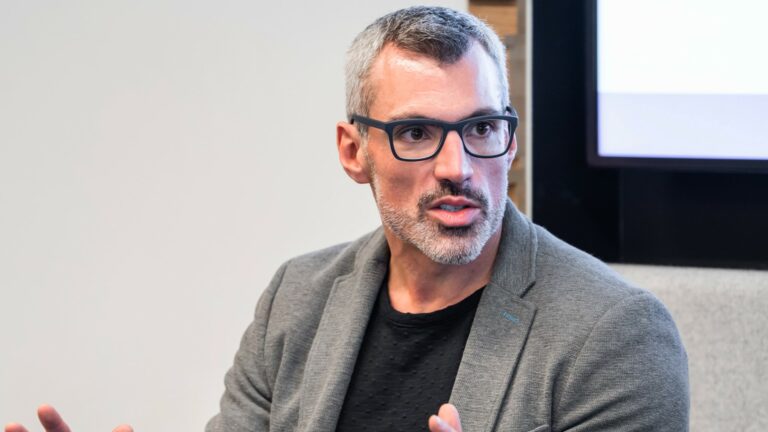 A man sits in a conference room talking and looking off-camera