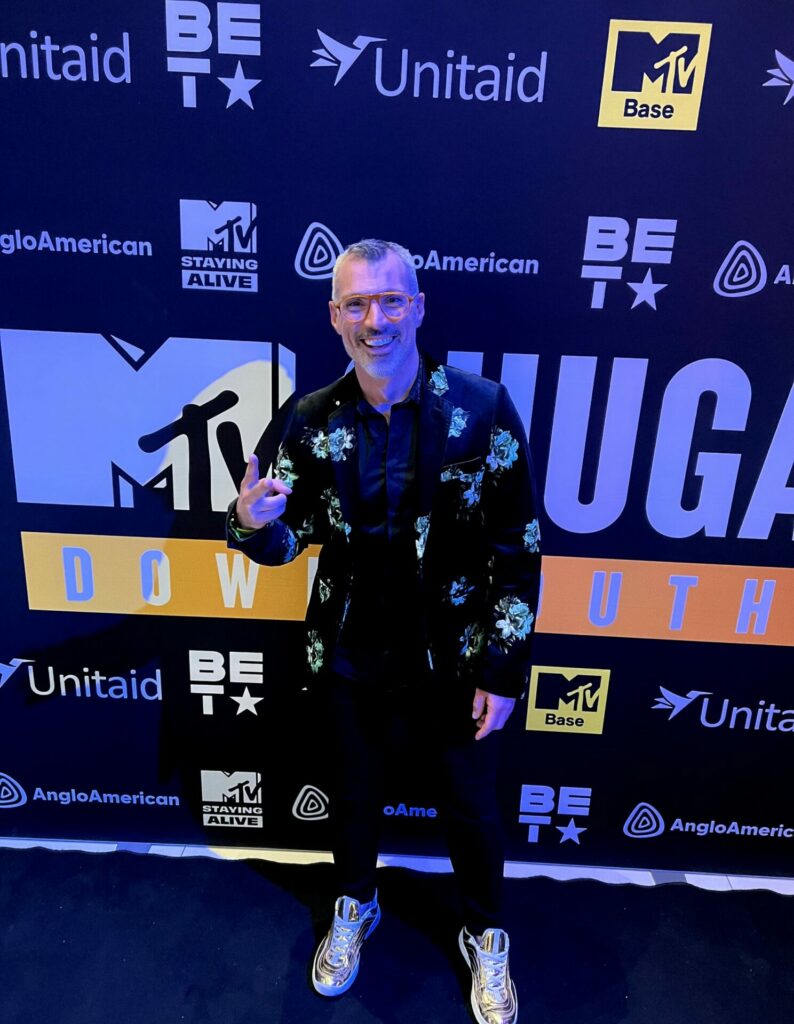 A man stands in front of a step and repeat board at an awards ceremony