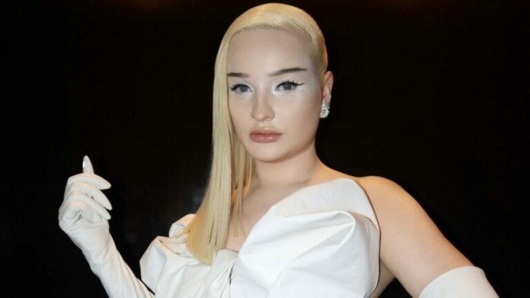 Kim Petras with blonde hair over her shoulder and a white dress and gloves.