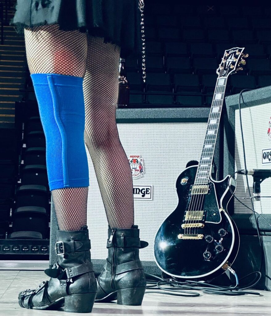 Close up of Madonna's legs on stage with a guitar in the background. She is wearing a blue bandage on her left knee