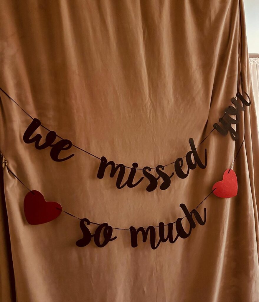 A brown curtain with a banner hanging on it which says "we missed you so much"