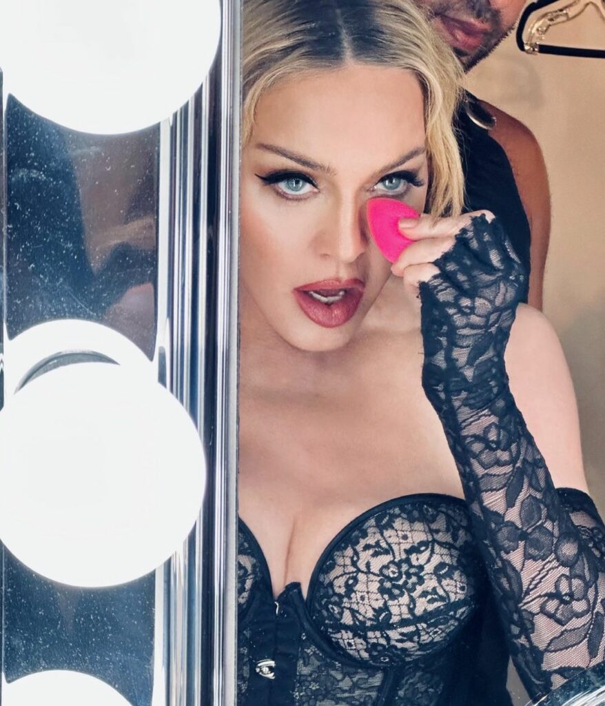 Madonna applies makeup to herself with a pink sponge in front of a makeup mirror