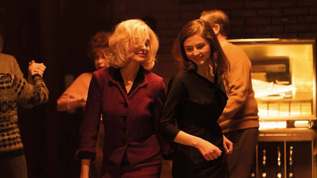 Eileen film still - Thomasin McKenzie and Anne Hathaway dancing.