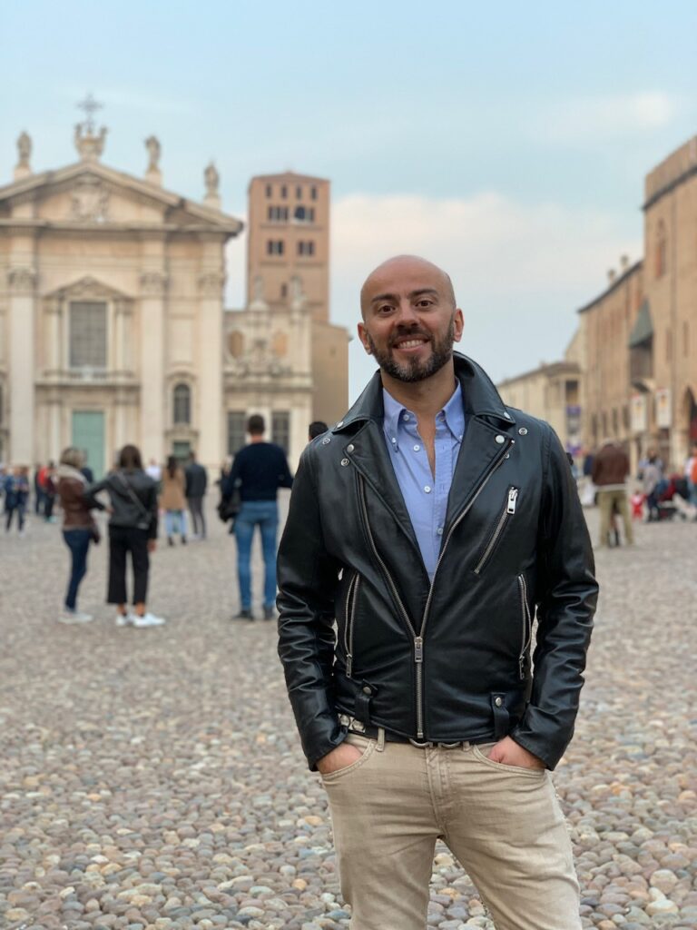 A smiling man stands in a European street