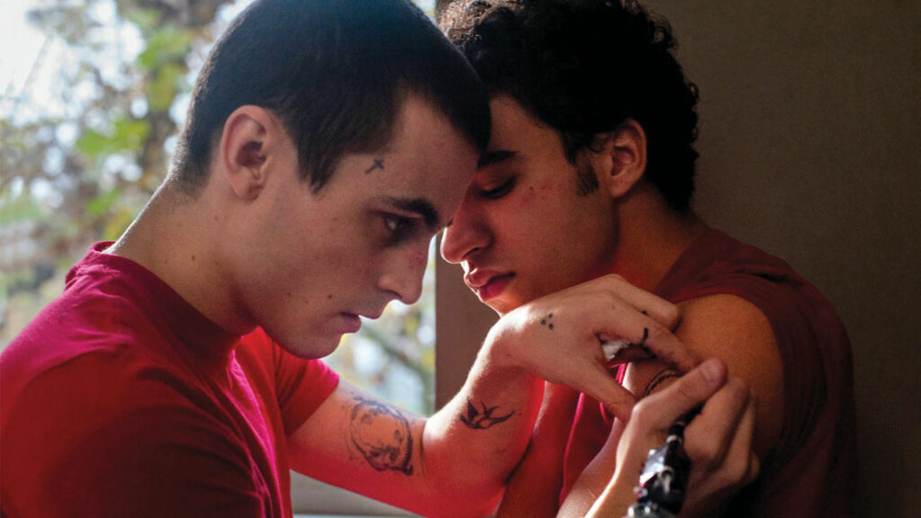 still fo The Lost Boys - one young tatttoed man tattooing another young man
