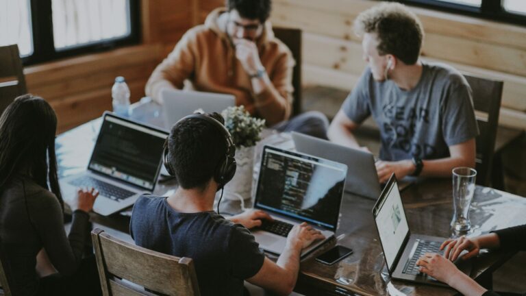 Five people sit around a desk using their laptops