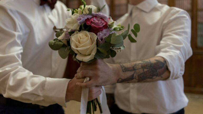 two men in white suits holding a wedding bouquet