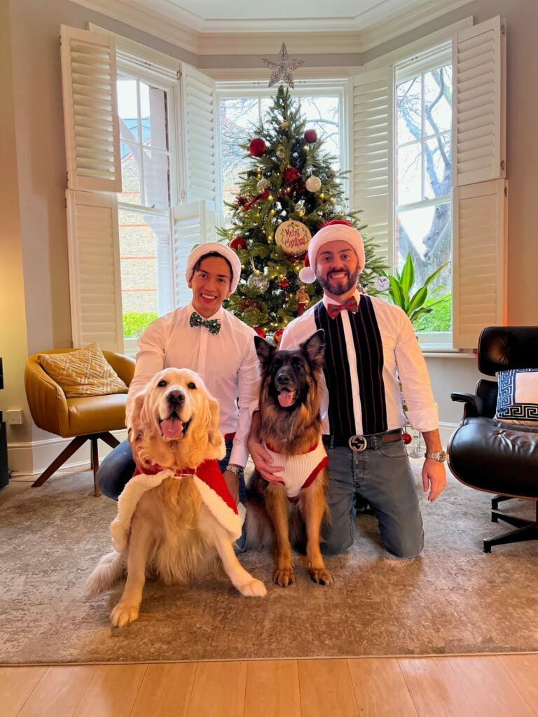 Two men and two dogs in front of a Christmas tree in a house
