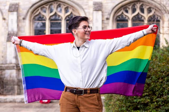 A person stands holding a Pride flag in outstretched arms
