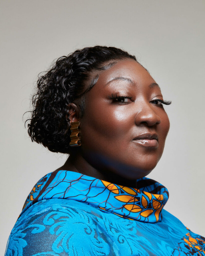 A black woman wearing a blue dress smiles into the camera