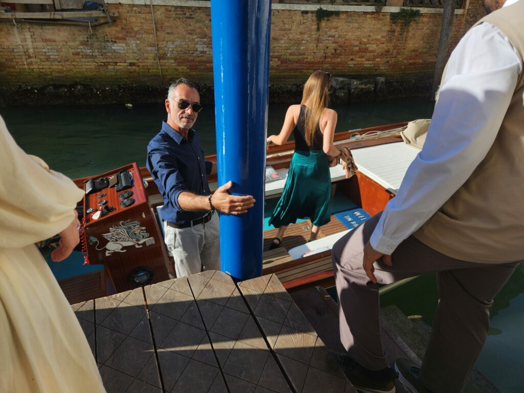 A skipper stands on a speedboat wearing a blue shirt and grey trousers and sunglasses